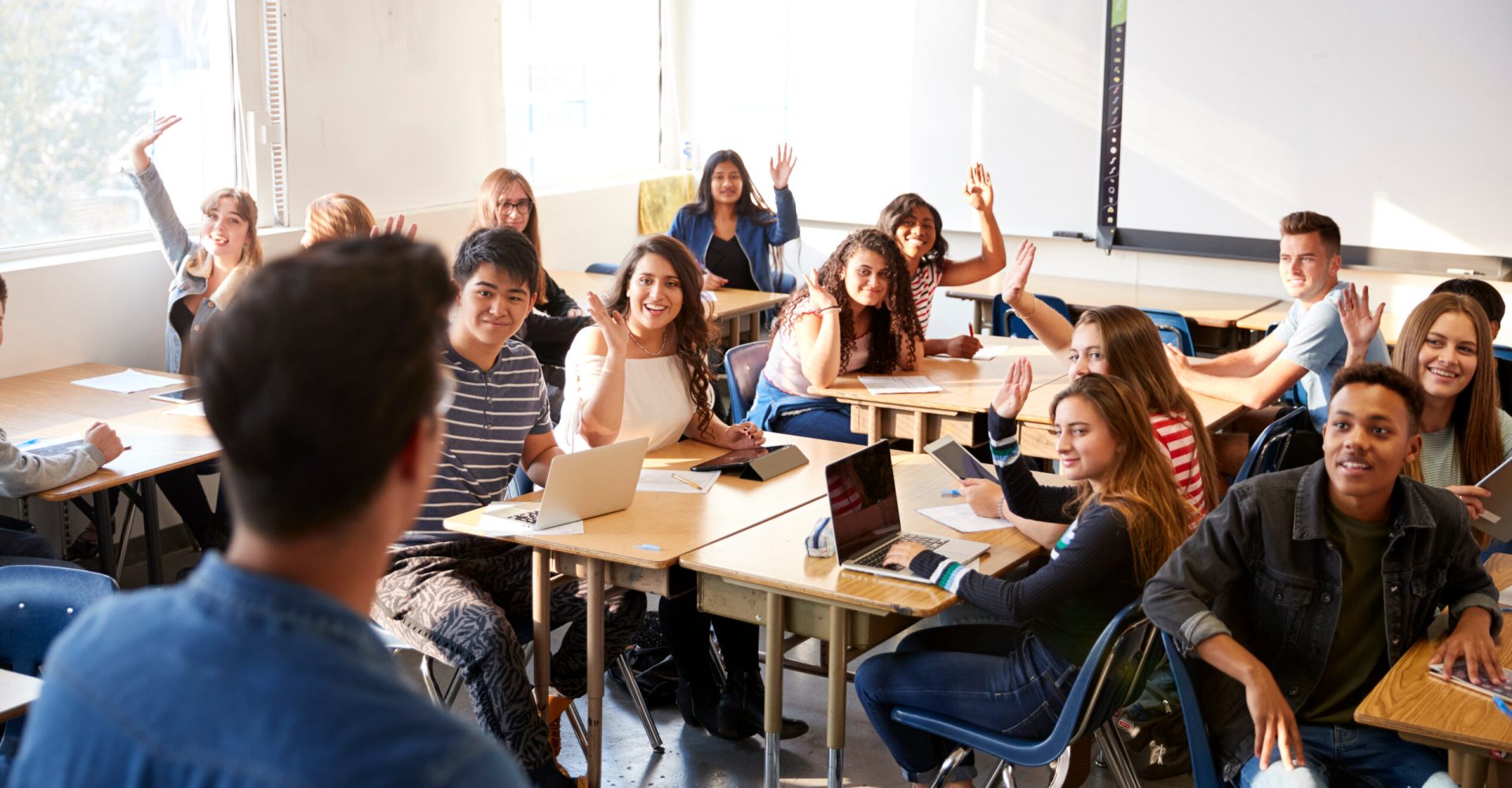 Rear View Of Male High School Teacher Standing At Front Of Class Teaching Lesson