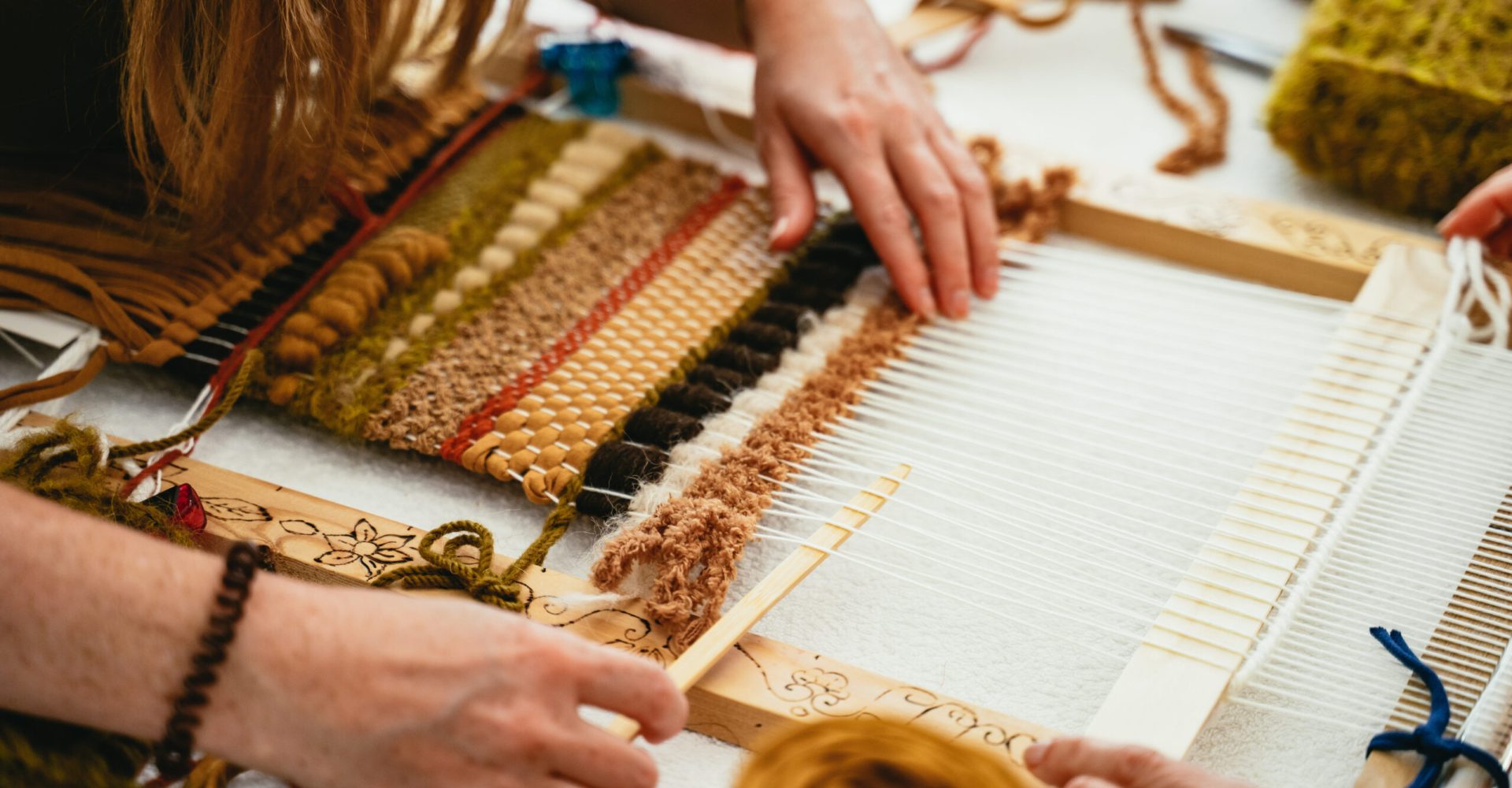 Woman trying her hand at weaving a tapestry during a class in a close up on her hands and the yarns on a small wooden hand loom