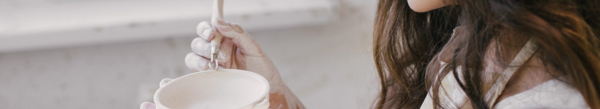 Young beautiful woman with long curly hair in white apron creating handmade ceramic bowl in a pottery. Creative workshop.