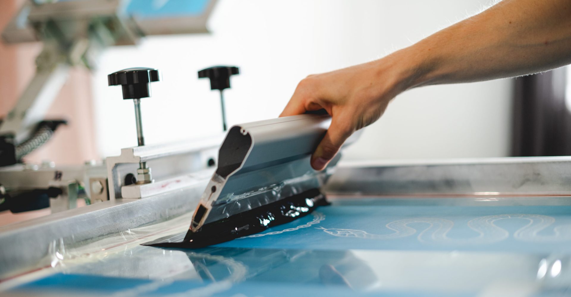 Cropped view of artisan holding squeegee with plastisol ink while working with screen printing machine in designer studio